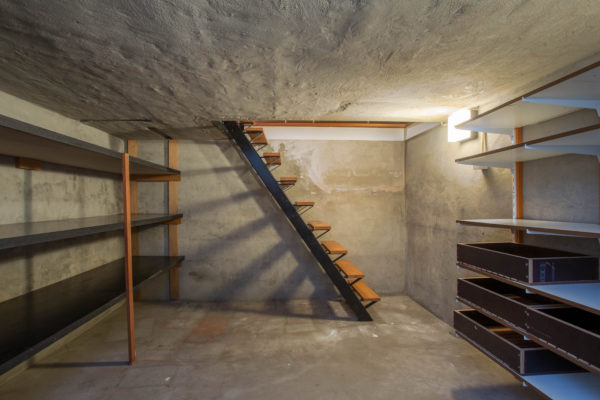 empty basement in abandoned old industrial building with little light and a wooden stairs and cement walls